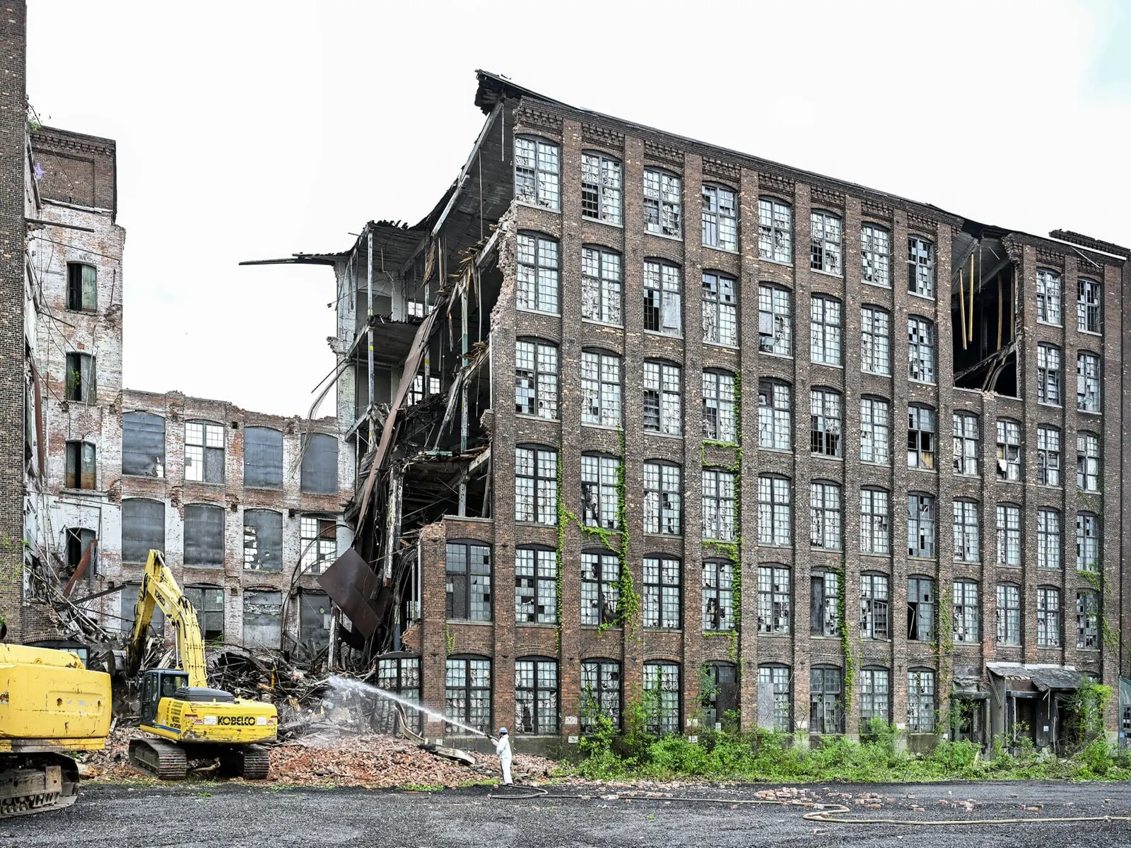 Excavators taking down a large brick mill building with the roof already opened up