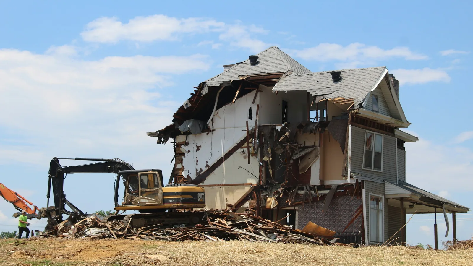Excavator taking down a large old farmhouse with a lumber debris pile below it