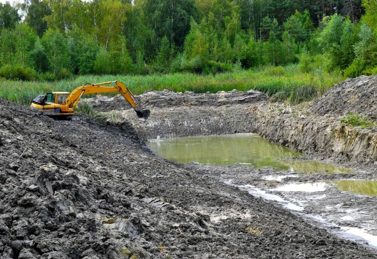 Excavator shaping the bank of a newly dug pond with water standing in the bottom