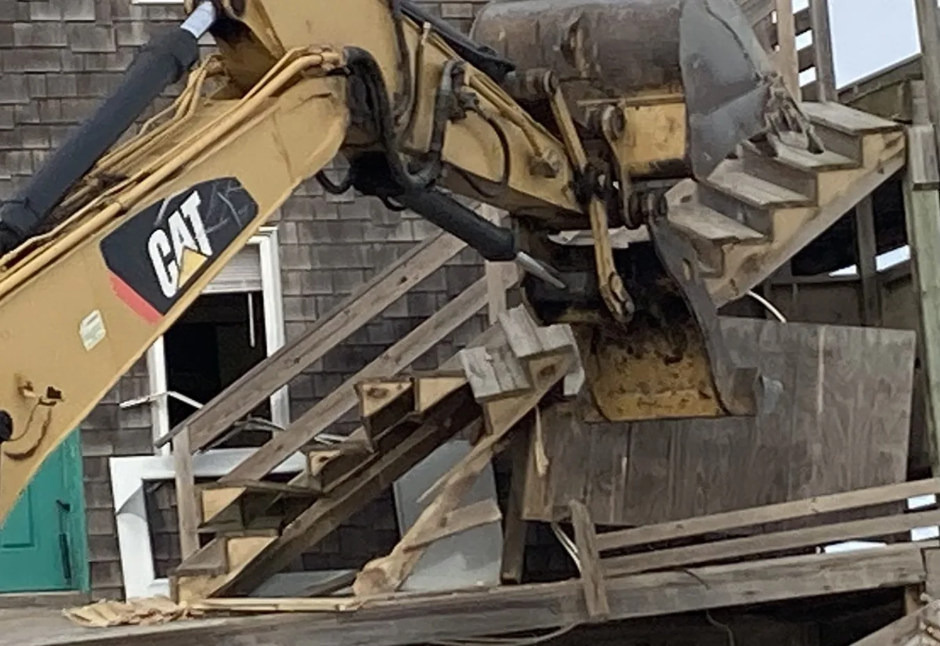 Excavator bucket pulling the stairs and siding off a shingled house