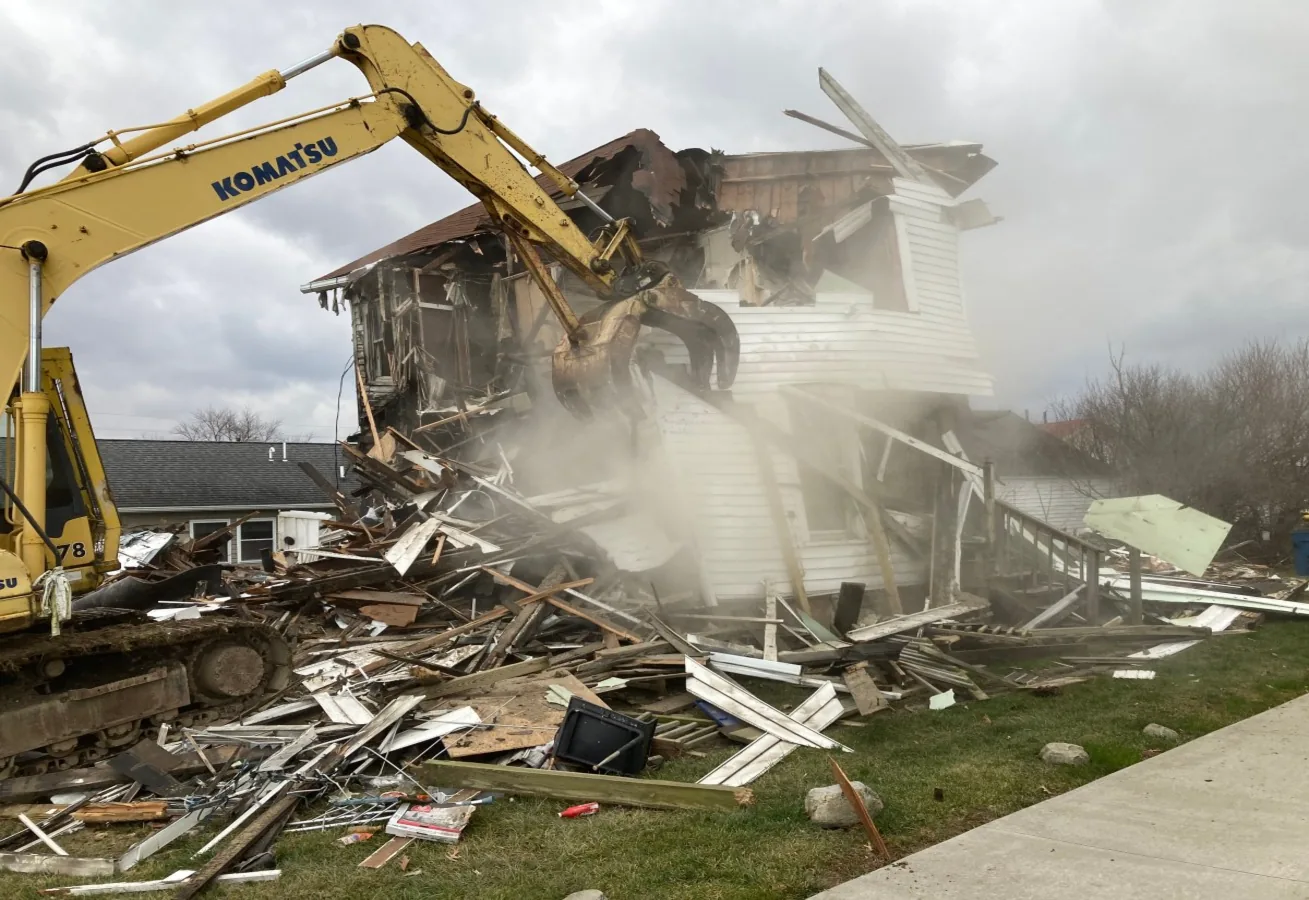 Two-story wood-frame house half torn down with a pile of splintered lumber in front of it