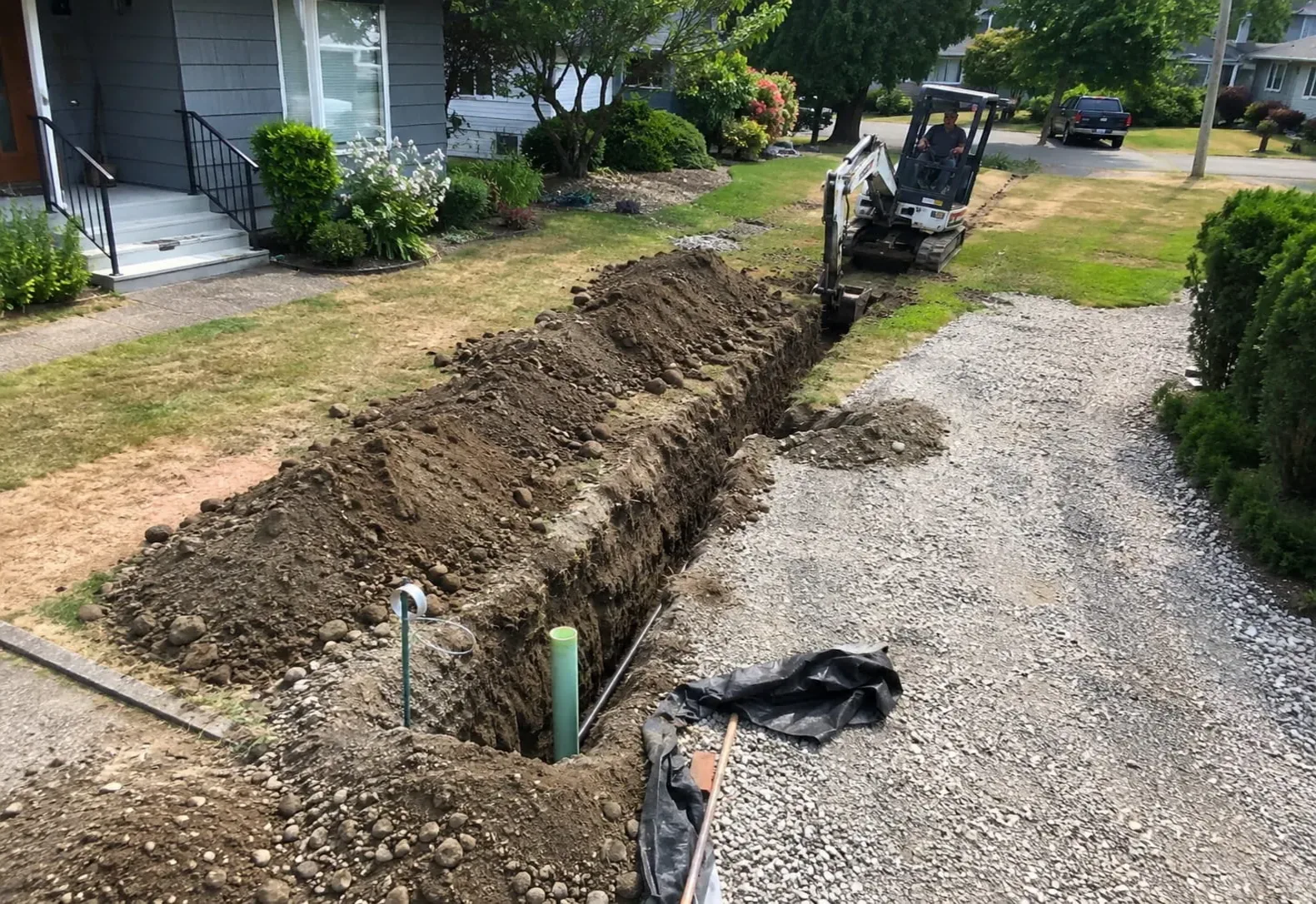 Trench running from a gravel driveway toward a house with conduit set in the bottom